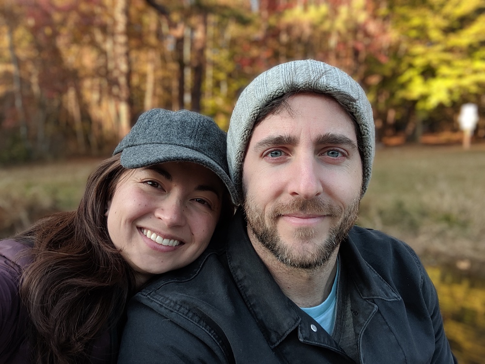 Robin and Max smiling in front of fall foliage